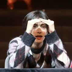 a woman covering her eyes while sitting in front of a table with an object on it