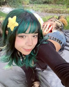 a woman with green hair laying on top of a bed next to a man in black shirt