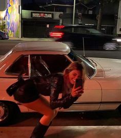 a woman leaning on the hood of a car while holding a cell phone in her hand