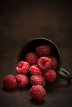 some raspberries are in a black bowl on a brown surface with dark background