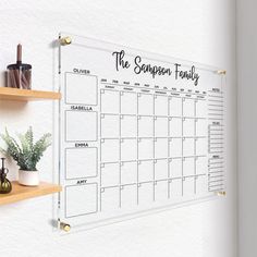 a wall calendar hanging on the side of a white wall next to two wooden shelves