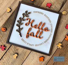 a wooden frame with the words hello fall on it and leaves scattered all around it