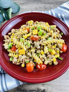 a red plate topped with pasta salad next to a blue and white striped napkin on top of a wooden table