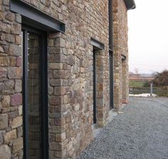 an old brick building with black glass doors and windows on the outside, along side gravel road