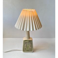 a lamp that is sitting on top of a white tablecloth with a beige shade