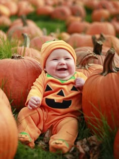 a baby sitting in the grass with pumpkins around him and smiling at the camera