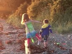 two young children are playing on the shore line with their arms around each other and holding hands