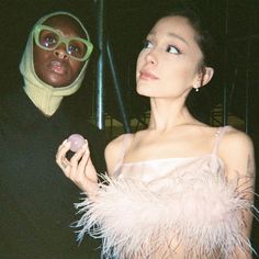 a woman standing next to a man in a black shirt and pink feathered dress