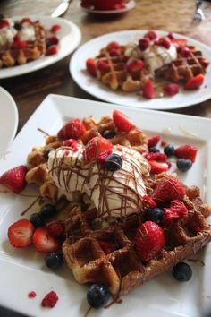 waffles with strawberries, blueberries and whip cream on them are sitting on plates