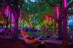 two people laying in hammocks under trees with colorful lights hanging from the branches