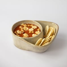 a bowl filled with soup and crackers on top of a white table next to a plate