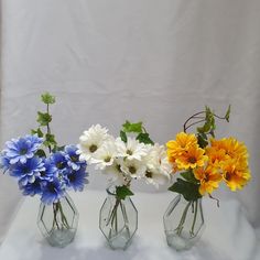 three vases filled with different colored flowers on a white tableclothed surface in front of a white backdrop