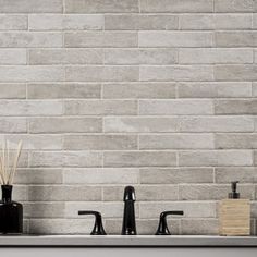 two black faucets sitting on top of a kitchen sink next to a white brick wall