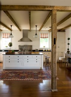 an open kitchen and dining room with wood beams on the ceiling, hardwood flooring