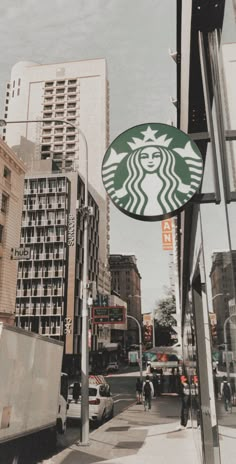 a starbucks sign hanging from the side of a building next to tall buildings in a city