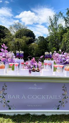 an outdoor bar decorated with purple flowers and wine glasses on the table for a cocktail party