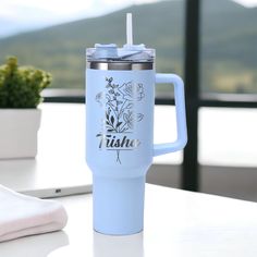 a blue travel mug sitting on top of a table next to a potted plant