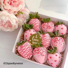 a box filled with lots of pink strawberries next to a bouquet of flowers and a sign that says i love you