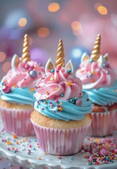 three cupcakes with pink and blue frosting, topped with unicorn - like decorations