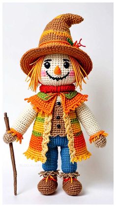 a crocheted scarecrow holding a stick and wearing a hat with an orange scarf