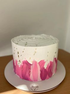 a white cake with pink flowers on it sitting on top of a wooden table next to a wall