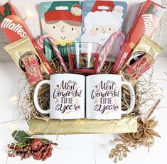 two coffee mugs filled with candy and candies are sitting in a gift box