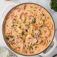 a pan filled with pasta and meatballs on top of a white table next to some parsley