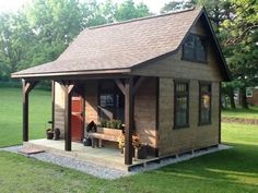 a small wooden cabin with a porch and covered front door in the grass next to trees