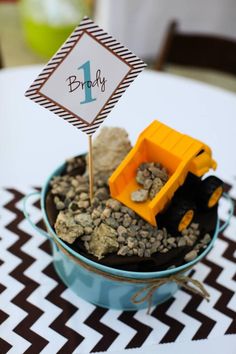 a table topped with a blue bowl filled with dirt and a yellow toy bulldozer