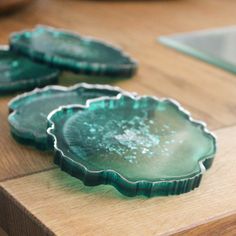 three green glass plates sitting on top of a wooden table next to a bowl filled with fruit