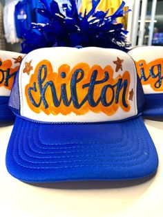 Everyone loves an original. That piece that no one else has. We've got you covered with our hand painted (and glittered) spirit truckers!  Cheer on your team or celebrate a bride-to-be or rock your favorite quote or hashtag ("slay")... these hats will surely have people asking, "where did you get that hat?" Our hats are constructed with rear mesh panels and a foam front. It features an integrated cotton sweatband, a pre-curved bill, and an adjustable plastic snap closure.  IMPORTANT NOTES:  No two hats will be the same. We do not use a template of any kind, so everything (placement, highlight, etc) is different.  We love to  customize hats for you with your choice of team/mascot and colors, even the color of the trucker, in some cases. Due to trademarking laws, some team names, sayings and Custom Hats Nashville, Painted Hats Diy, Painted Trucker Hats, Paint Games, Painted Hats, Team Mascots, Diy Hat, Painted Letters, Custom Hand Painted