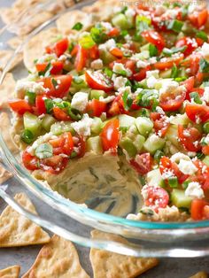 a glass bowl filled with cucumber, tomatoes and feta cheese on crackers