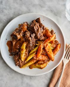 a white plate topped with beef and carrots next to a fork on a table