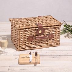 a wicker picnic basket next to a glass of wine