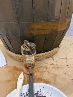 a wooden bucket filled with dirt next to a metal spoon and some brown stuff on the ground