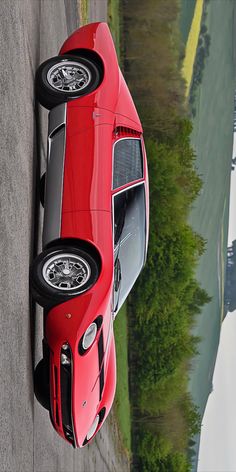 a red sports car parked on the side of a road next to a body of water