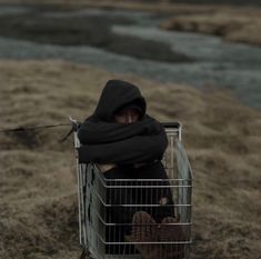 a person sitting in a shopping cart on the side of a road with their arms wrapped up