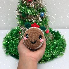 a hand holding a small stuffed animal in front of a christmas tree with ornaments on it