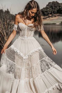 a woman in a white dress is standing by the water