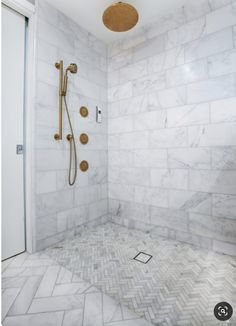 a walk in shower sitting next to a white tiled wall and floor with gold fixtures