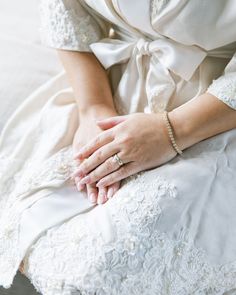 a woman sitting on top of a bed wearing a white dress and holding her hands together