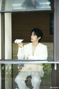 a man in white suit sitting at a window sill holding a piece of paper