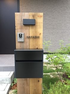 a mailbox sitting on top of a wooden post in front of a building with the word hayashi written on it