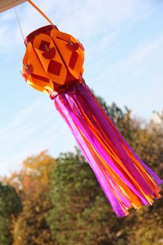 an orange and pink kite hanging from the side of a building with trees in the background