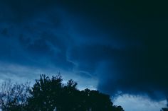 the sky is dark and cloudy with some trees in the foreground at night time