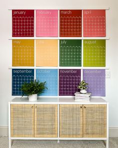 a colorful calendar is on the wall behind a white sideboard with wicker drawers