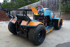 an orange and blue vehicle parked on top of a cement lot next to a wooden fence