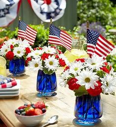 red, white and blue flowers in vases sitting on a table with american flags