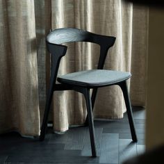 a black chair sitting in front of a window next to a wooden floor and curtain