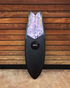 a black surfboard sitting against a wooden wall